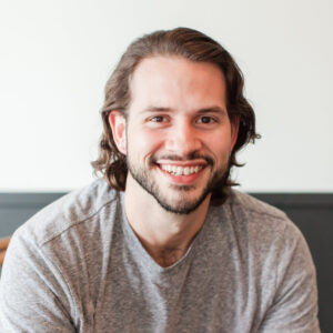 Smiling man with brown hair and a beard wearing a gray t-shirt.